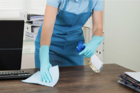 Person cleaning an office desk with a cloth and spray bottle