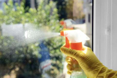 Person cleaning window with spray bottle wearing yellow gloves