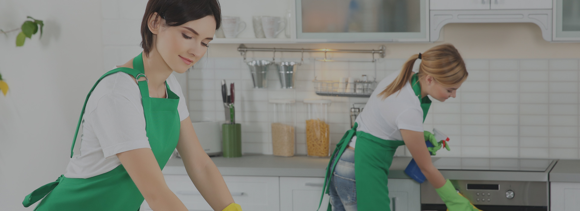 Women cleaning a modern kitchen with green aprons and gloves