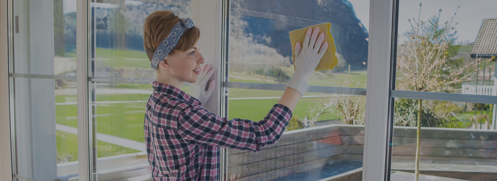 Woman cleaning a glass window with a sponge in a sunny room