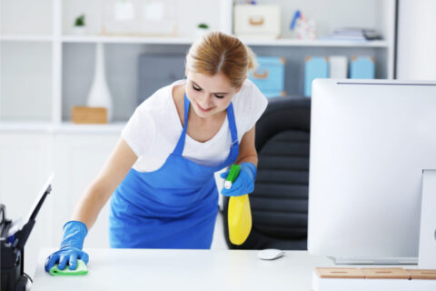 Office worker cleaning desk with spray bottle and cloth